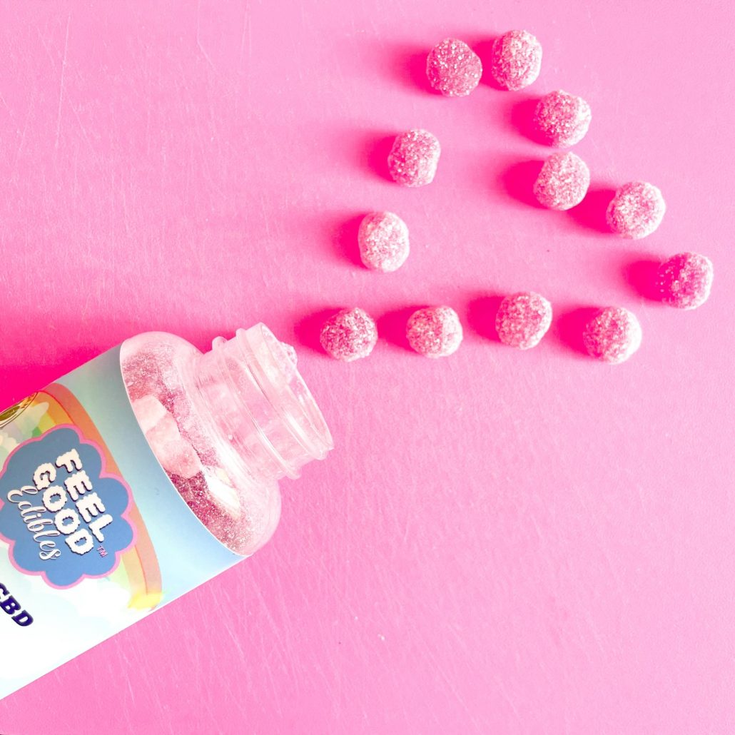 Colorful CBD gummy edibles spilling from a bottle, arranged in a heart shape on a pink background.
