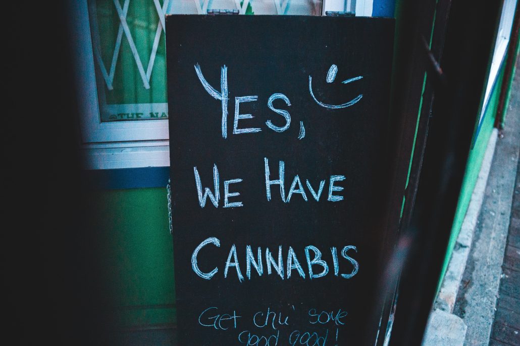 A chalkboard sign welcoming customers and advertising the availability of cannabis products.