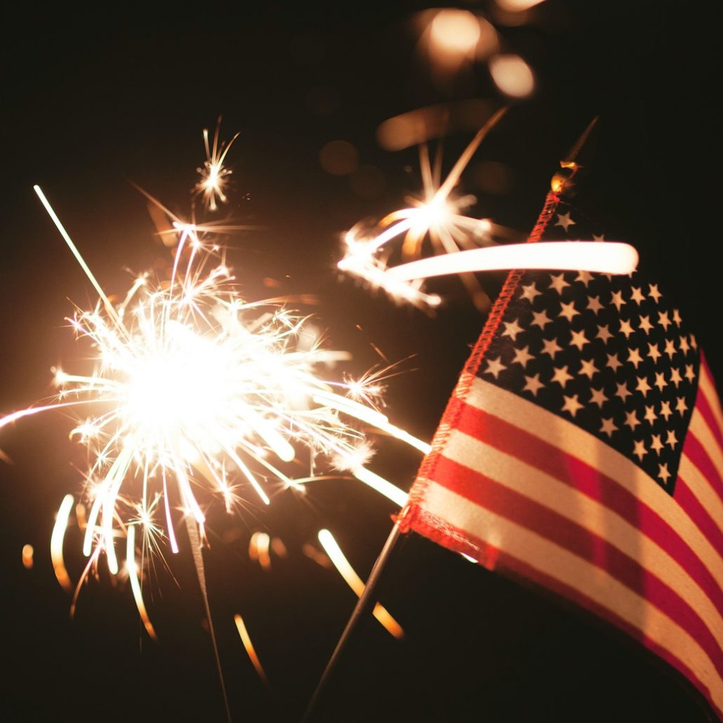 An American flag surrounded by sparklers against a dark background, capturing the festive spirit of the 4th of July.