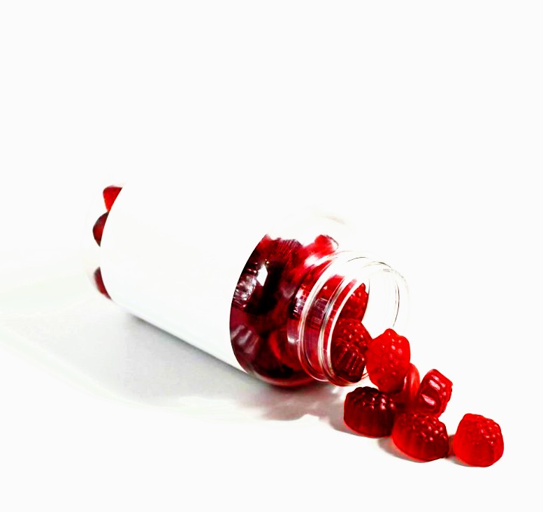 Red raspberry CBD gummies spilling from a clear bottle on a white background, complementing food pairings.
